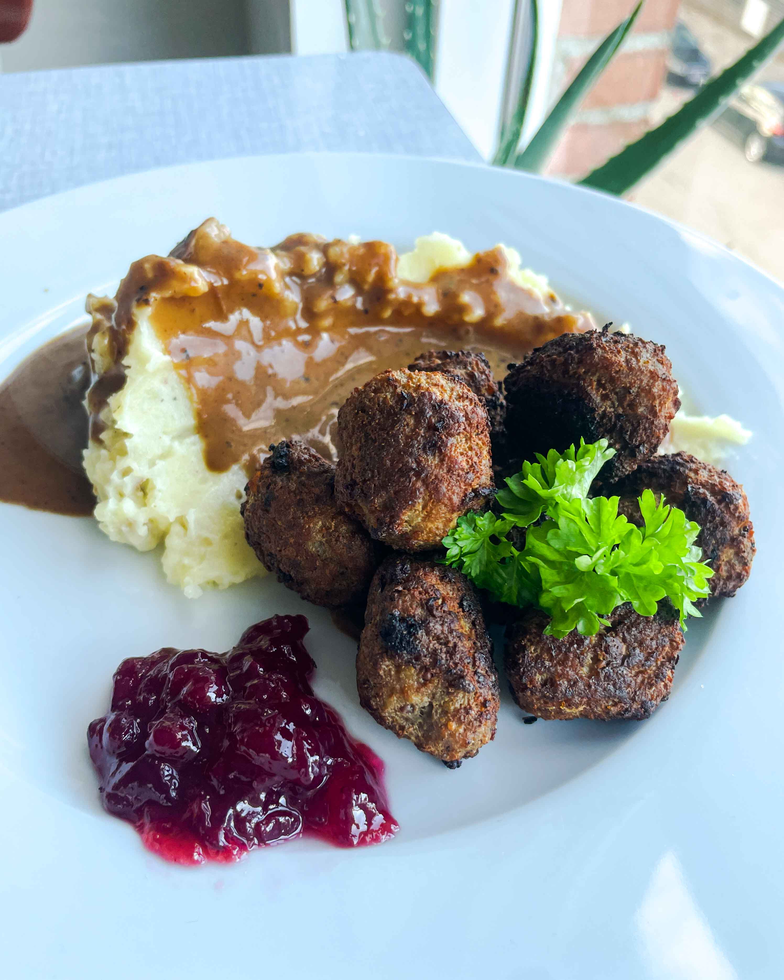 Saftige svenske kødboller hviler på en seng af cremet kartoffelmos, toppet med et strejf af farverigt tyttebærsyltetøj. En smagsoplevelse og visuel fest i én bid!