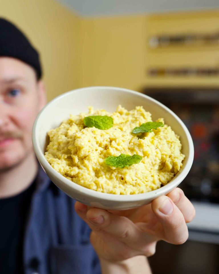 En skål fyldt med cremet hummus, dekoreret med friske mynteblade på toppen, der tilføjer en frisk og aromatisk touch til den lækre kikærtebaserede dip