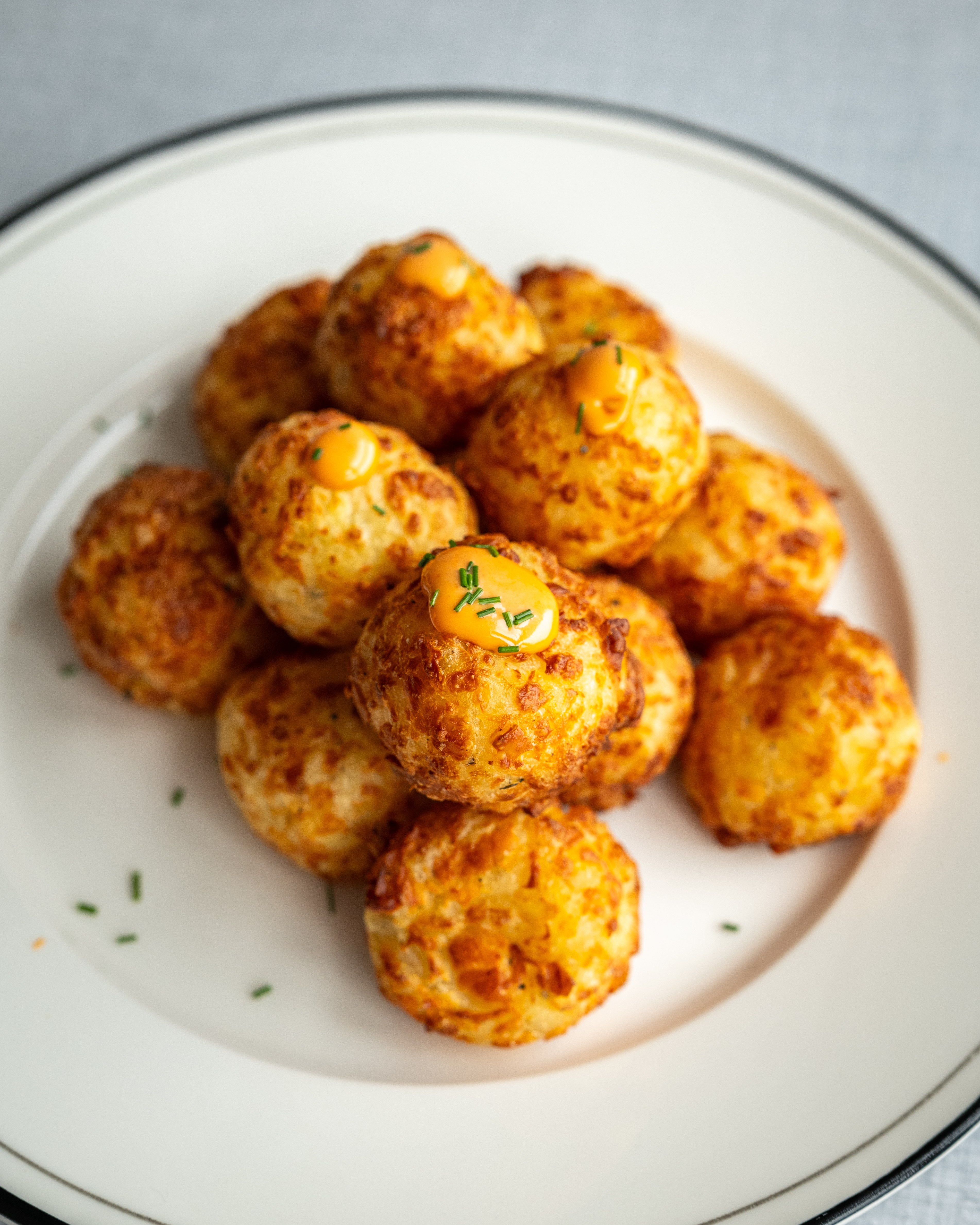 Sprøde kartoffelkugler med halloumi serveret på en tallerken med chilimayo ved siden af.