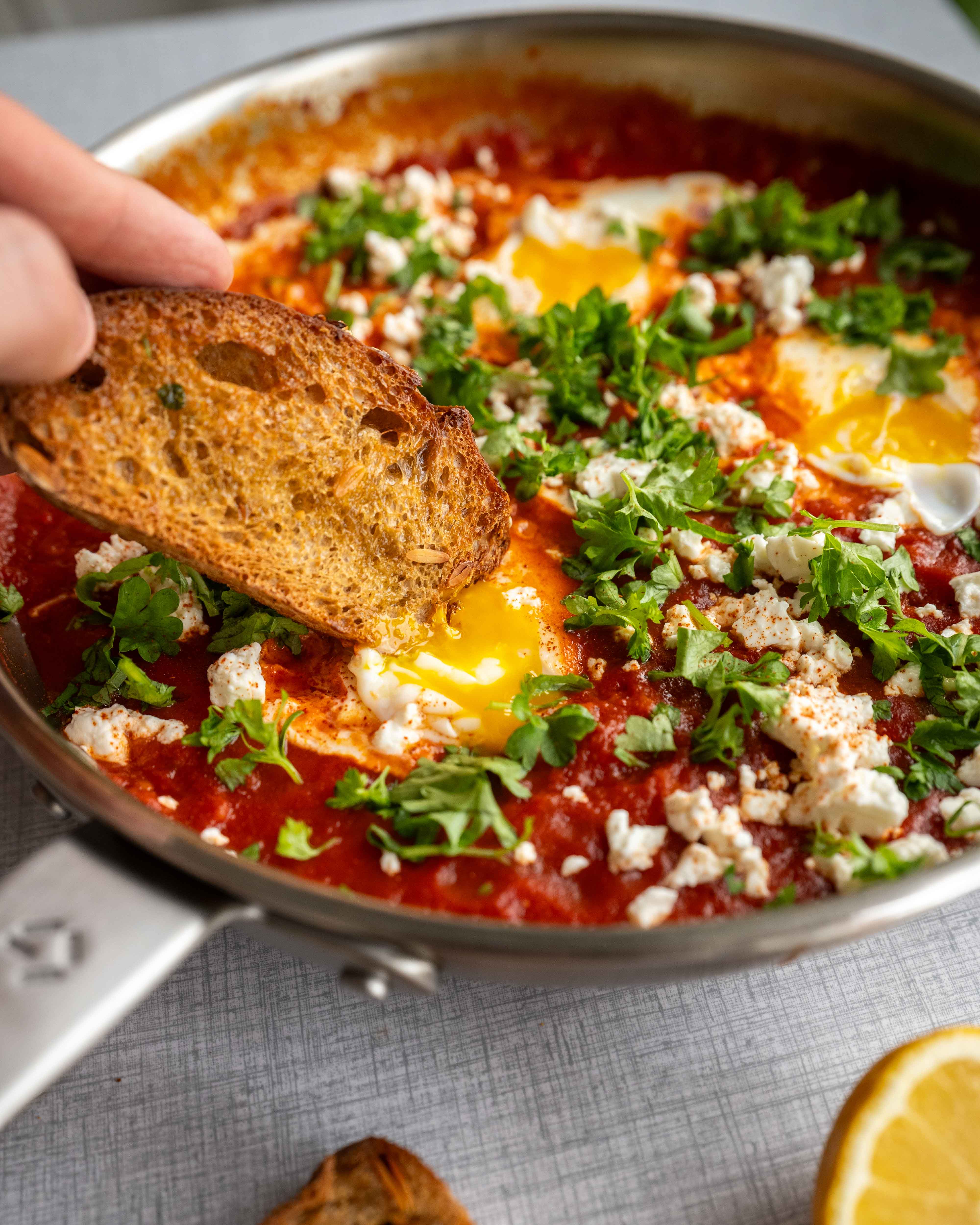 En pande shakshuka med æg, krydret tomatsauce og stykker af sucuk, toppet med friske krydderurter.