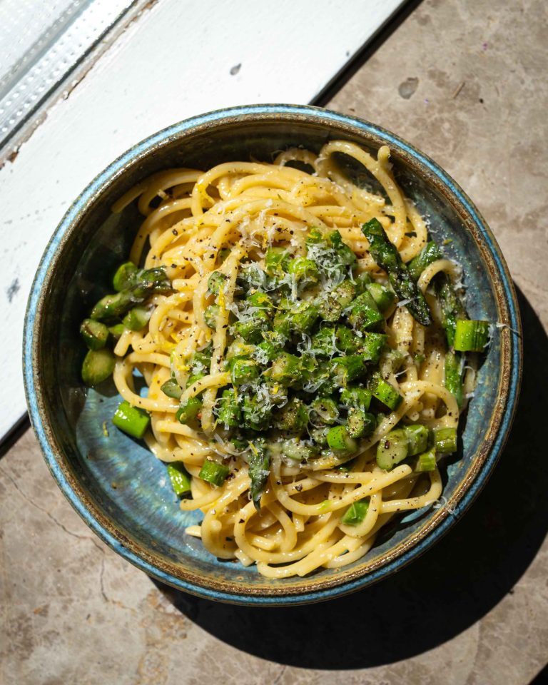 Cremet asparges carbonara med grønne asparges, pecorino, citron og sort peber serveret i en dyb tallerken.